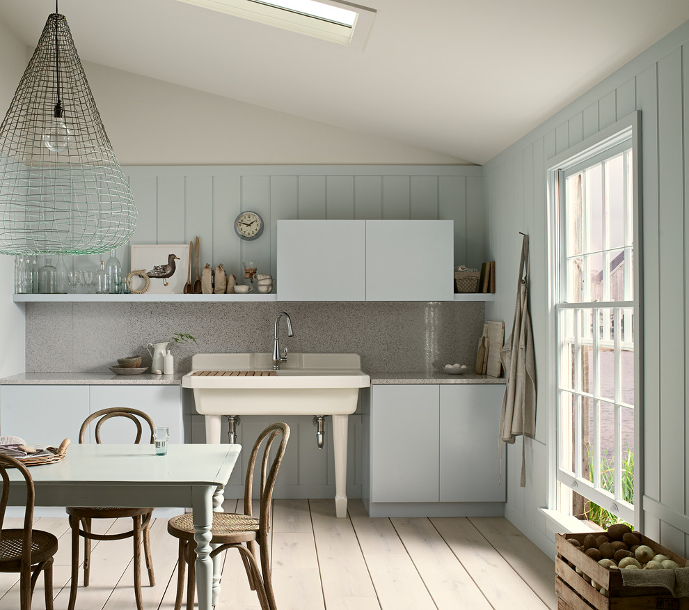 Inspiration for a mid-sized beach style single-wall eat-in kitchen in Milwaukee with a farmhouse sink, flat-panel cabinets, blue cabinets, quartz benchtops, grey splashback, stone slab splashback, light hardwood floors, no island and beige floor.