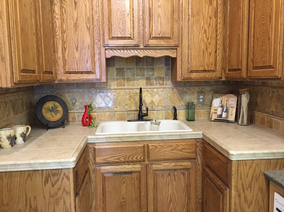This is an example of a small traditional u-shaped separate kitchen in Other with tile benchtops, beige splashback, travertine splashback, porcelain floors, a drop-in sink, raised-panel cabinets, medium wood cabinets, black appliances, no island and beige floor.