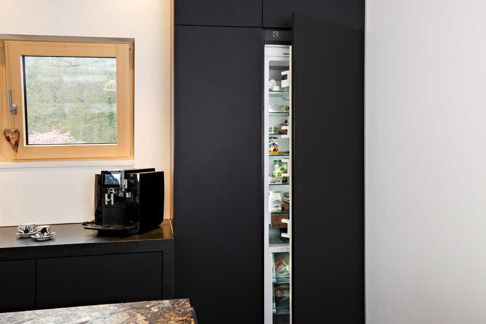Inspiration for a large modern galley eat-in kitchen in Stuttgart with an undermount sink, flat-panel cabinets, black cabinets, granite benchtops, white splashback, window splashback, black appliances, cement tiles, with island, black floor and black benchtop.