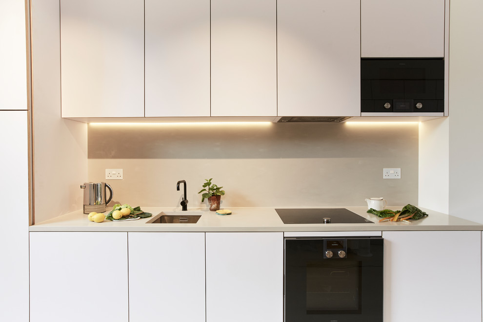 Design ideas for a small modern single-wall open plan kitchen in London with an integrated sink, flat-panel cabinets, beige cabinets, solid surface benchtops, black appliances and beige benchtop.