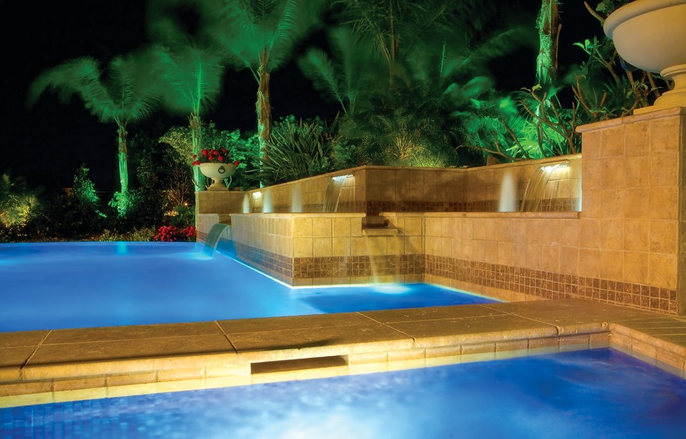 Large tropical backyard rectangular pool in Miami with a water feature and natural stone pavers.