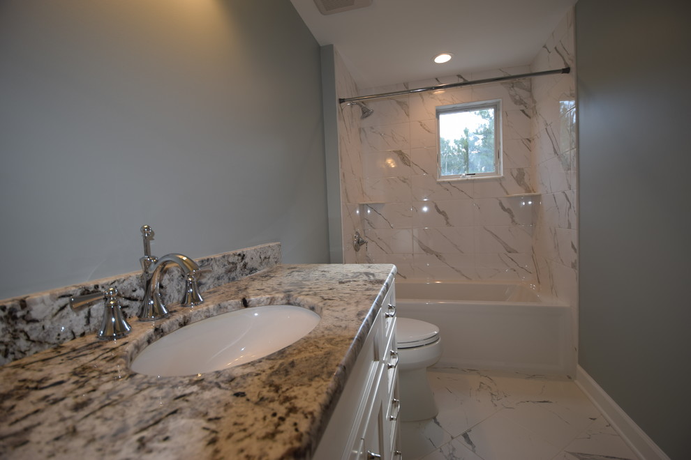 Photo of a mid-sized beach style 3/4 bathroom in Philadelphia with recessed-panel cabinets, white cabinets, an alcove tub, an alcove shower, a two-piece toilet, gray tile, white tile, marble, grey walls, marble floors, an undermount sink, glass benchtops, white floor and a shower curtain.