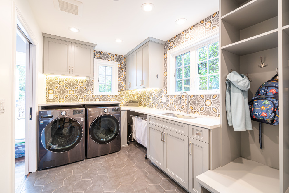 Large traditional u-shaped utility room in Seattle with a submerged sink, grey cabinets, engineered stone countertops, a side by side washer and dryer, grey floors, white worktops, flat-panel cabinets, grey splashback, ceramic splashback, multi-coloured walls and ceramic flooring.