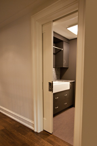 This is an example of a large modern galley dedicated laundry room in Toronto with a farmhouse sink, flat-panel cabinets, dark wood cabinets, white walls, granite benchtops, multi-coloured splashback, granite splashback, vinyl floors, a concealed washer and dryer, brown floor and multi-coloured benchtop.