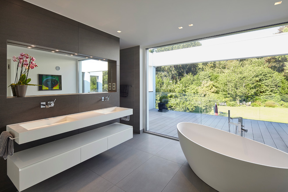 Design ideas for a modern master bathroom in Dusseldorf with flat-panel cabinets, white cabinets, a freestanding tub, gray tile, solid surface benchtops, cement tile and an integrated sink.