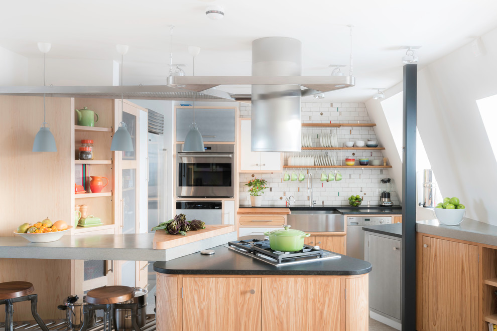 This is an example of a contemporary u-shaped open plan kitchen in London with a farmhouse sink, flat-panel cabinets, light wood cabinets, concrete benchtops, white splashback, stainless steel appliances and a peninsula.