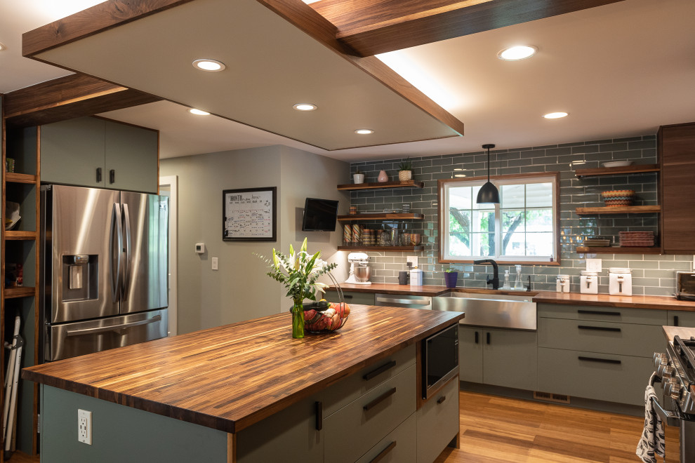 This is an example of a mid-sized transitional u-shaped kitchen pantry in Denver with a farmhouse sink, flat-panel cabinets, green cabinets, wood benchtops, green splashback, glass tile splashback, stainless steel appliances, medium hardwood floors, with island, brown floor, brown benchtop and exposed beam.
