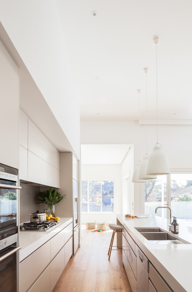 Photo of a mid-sized contemporary galley eat-in kitchen in Sydney with an undermount sink, flat-panel cabinets, beige cabinets, solid surface benchtops, grey splashback, stainless steel appliances, medium hardwood floors, with island, brown floor and porcelain splashback.