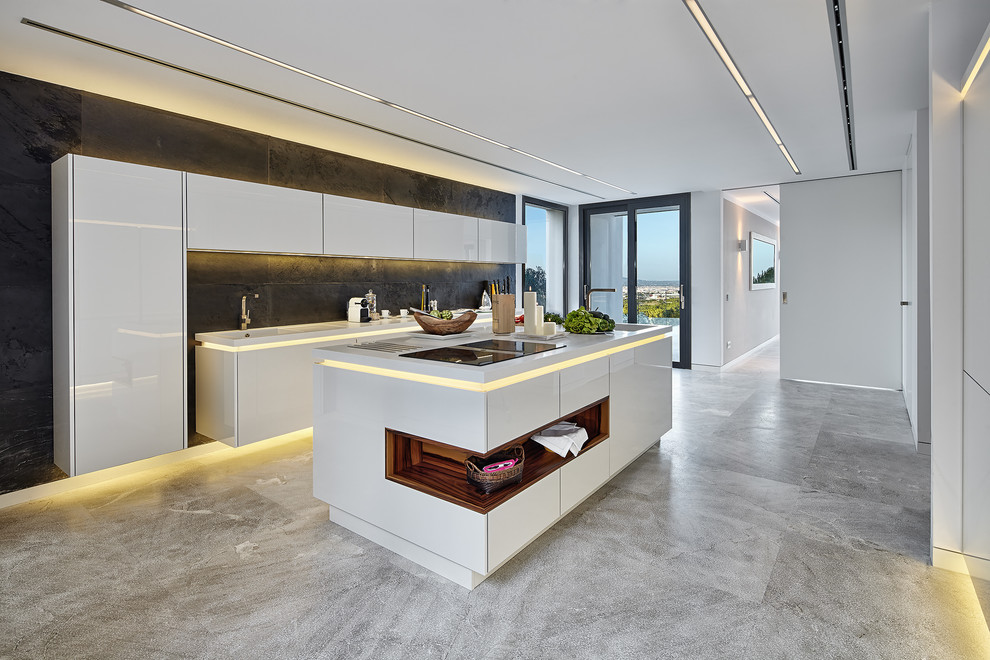 Design ideas for a large contemporary galley kitchen in Palma de Mallorca with an integrated sink, flat-panel cabinets, white cabinets, solid surface benchtops, black splashback, slate splashback, stainless steel appliances, limestone floors, with island, white benchtop and grey floor.