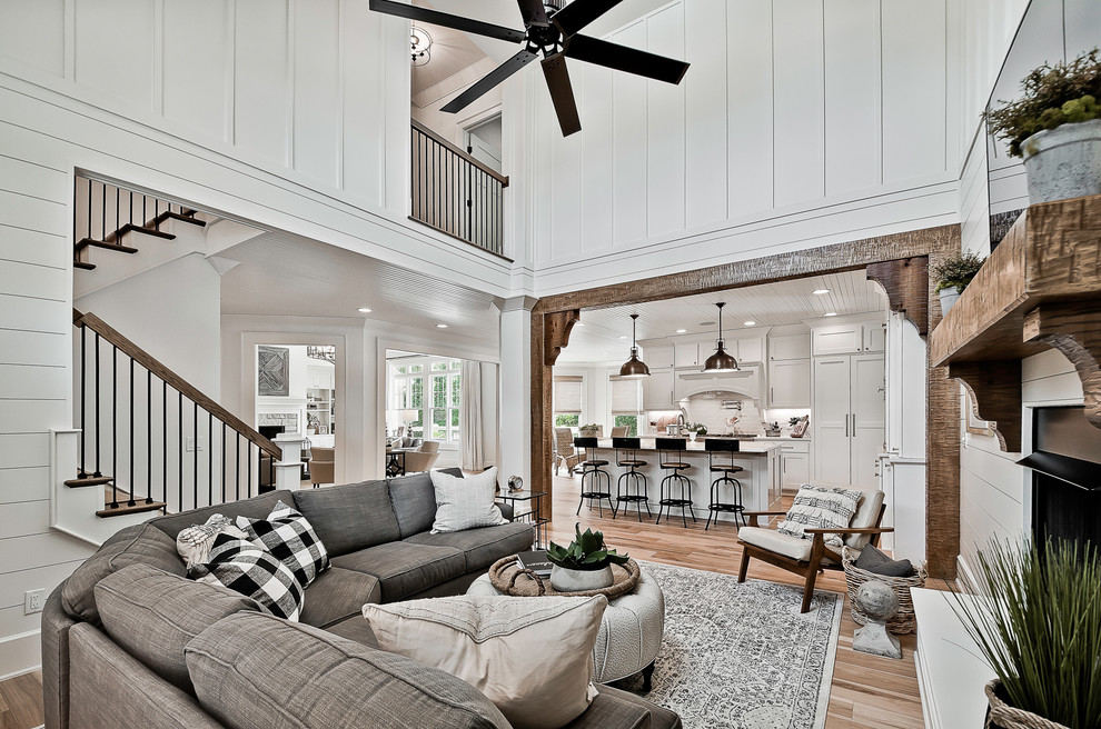 Design ideas for a country open concept living room in Other with white walls, medium hardwood floors, a standard fireplace, a wall-mounted tv and brown floor.