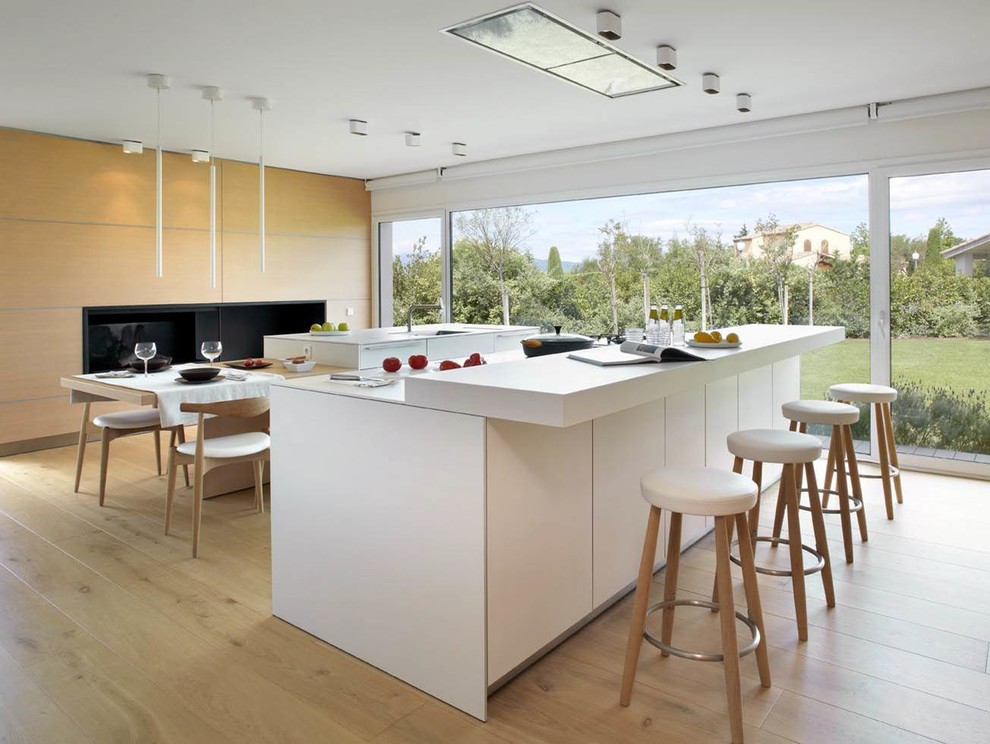 This is an example of a large contemporary eat-in kitchen in Other with flat-panel cabinets, white cabinets, solid surface benchtops, stainless steel appliances, light hardwood floors and multiple islands.