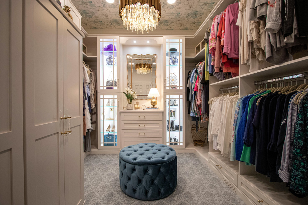 This is an example of a mid-sized traditional women's walk-in wardrobe in Cleveland with flat-panel cabinets, white cabinets, carpet, grey floor and wallpaper.
