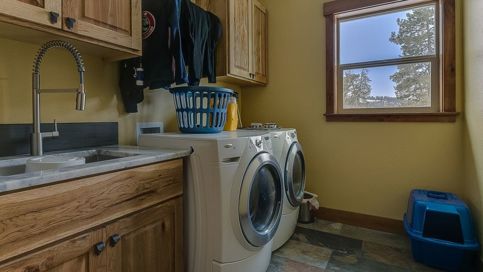 Photo of a mid-sized country single-wall dedicated laundry room in Seattle with an undermount sink, raised-panel cabinets, medium wood cabinets, marble benchtops, beige walls, slate floors, a side-by-side washer and dryer, multi-coloured floor and grey benchtop.