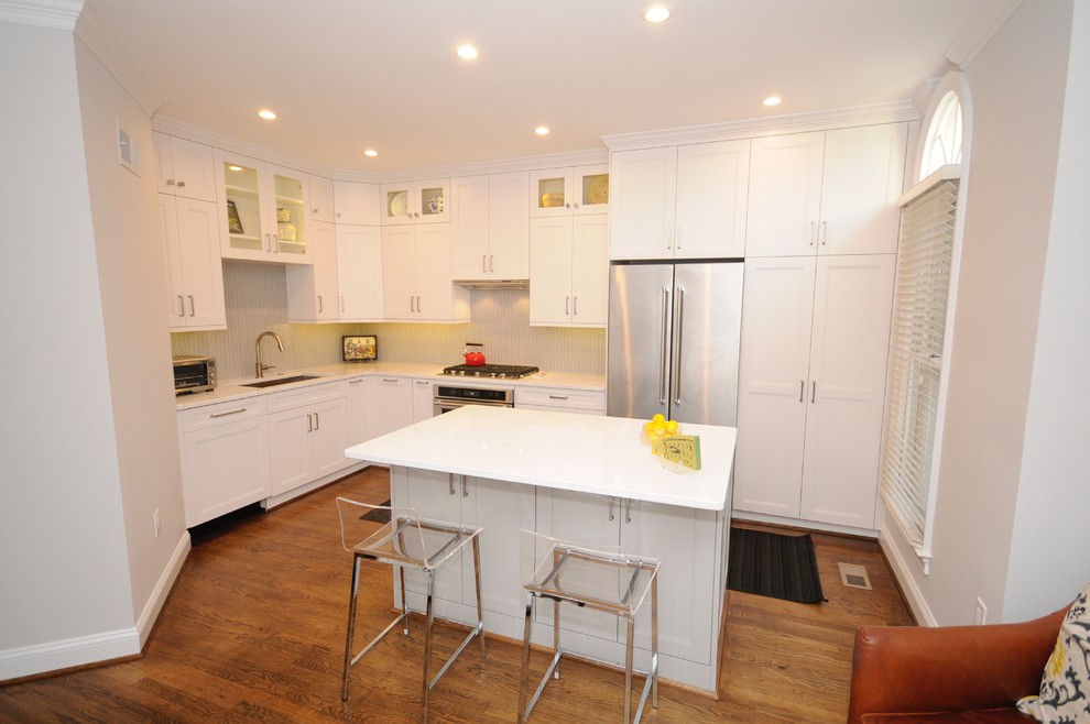 Example of a mid-sized transitional l-shaped medium tone wood floor eat-in kitchen design in DC Metro with a single-bowl sink, recessed-panel cabinets, white cabinets, quartz countertops, white backsplash, mosaic tile backsplash, stainless steel appliances and an island