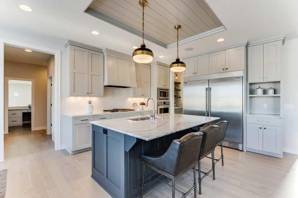 Inspiration for a transitional kitchen in Minneapolis with an undermount sink, recessed-panel cabinets, grey cabinets, white splashback, stainless steel appliances, light hardwood floors, with island, beige floor and white benchtop.