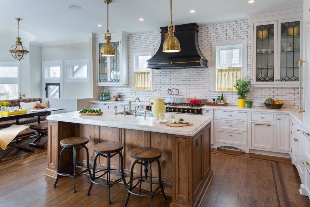 Ornate l-shaped medium tone wood floor eat-in kitchen photo in New York with an undermount sink, glass-front cabinets, white cabinets, white backsplash, subway tile backsplash, black appliances and an island