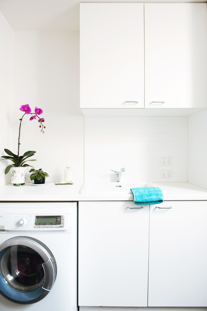 This is an example of a large contemporary single-wall utility room in Melbourne with a single-bowl sink, flat-panel cabinets, white cabinets, quartz benchtops, white walls, ceramic floors, a side-by-side washer and dryer and white benchtop.