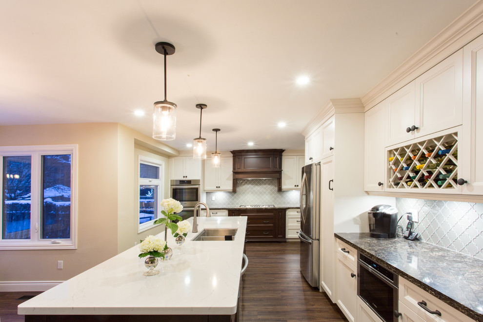 Large transitional l-shaped dark wood floor eat-in kitchen photo in Orange County with a double-bowl sink, recessed-panel cabinets, white cabinets, granite countertops, gray backsplash, glass tile backsplash, stainless steel appliances and an island