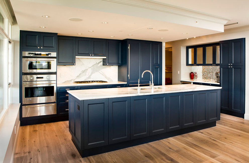 Design ideas for a mid-sized transitional l-shaped open plan kitchen in Vancouver with an undermount sink, recessed-panel cabinets, blue cabinets, marble benchtops, white splashback, marble splashback, stainless steel appliances, medium hardwood floors, with island and brown floor.