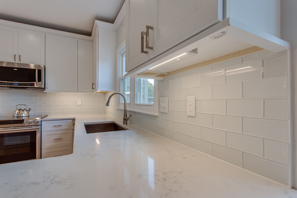 Example of a large transitional u-shaped light wood floor and brown floor open concept kitchen design in DC Metro with an undermount sink, shaker cabinets, white cabinets, solid surface countertops, white backsplash, glass tile backsplash, stainless steel appliances and a peninsula