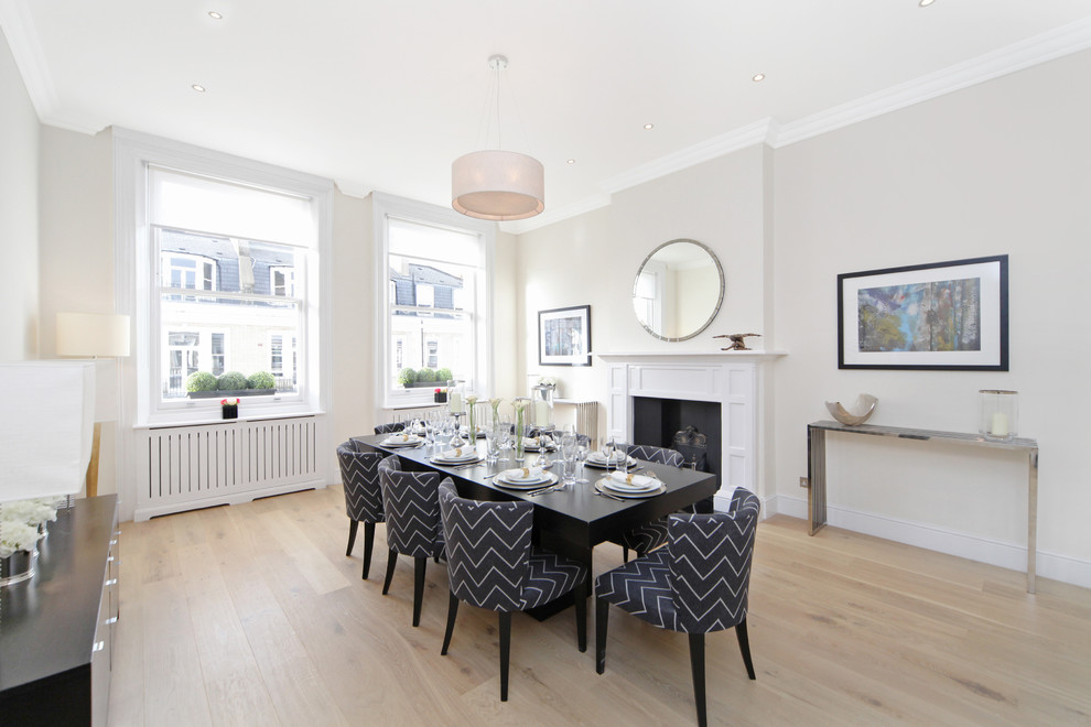 Photo of a large contemporary kitchen/dining combo in London with light hardwood floors, a standard fireplace, a wood fireplace surround and beige walls.