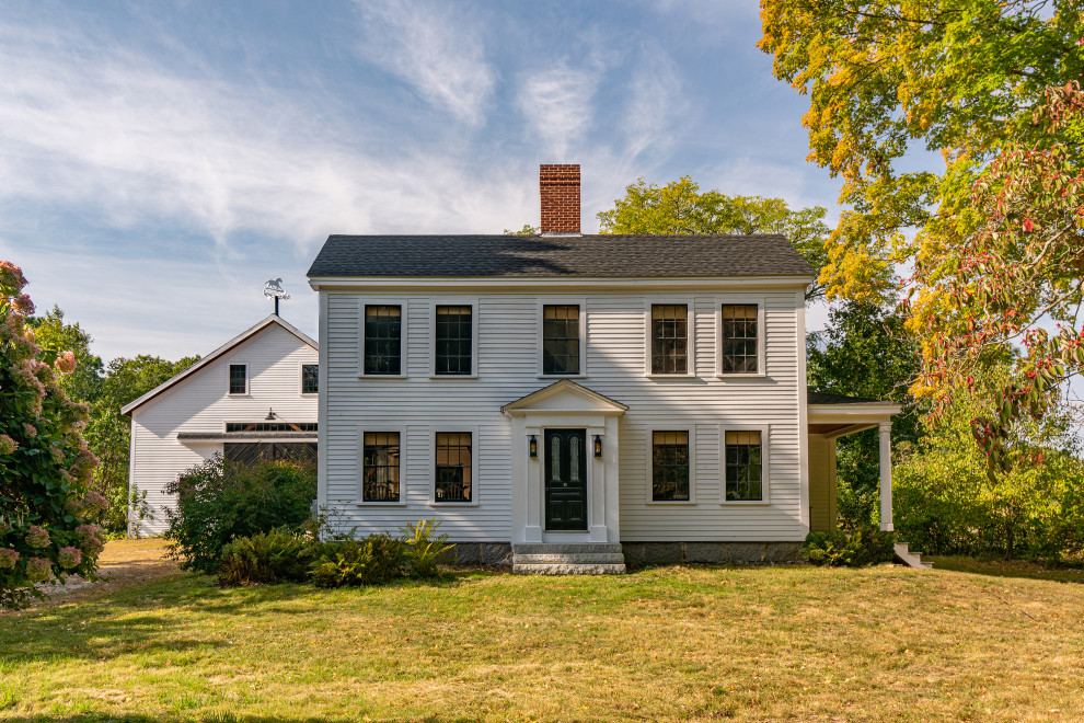 Photo of a country two-storey white house exterior in Boston with wood siding, a black roof and clapboard siding.