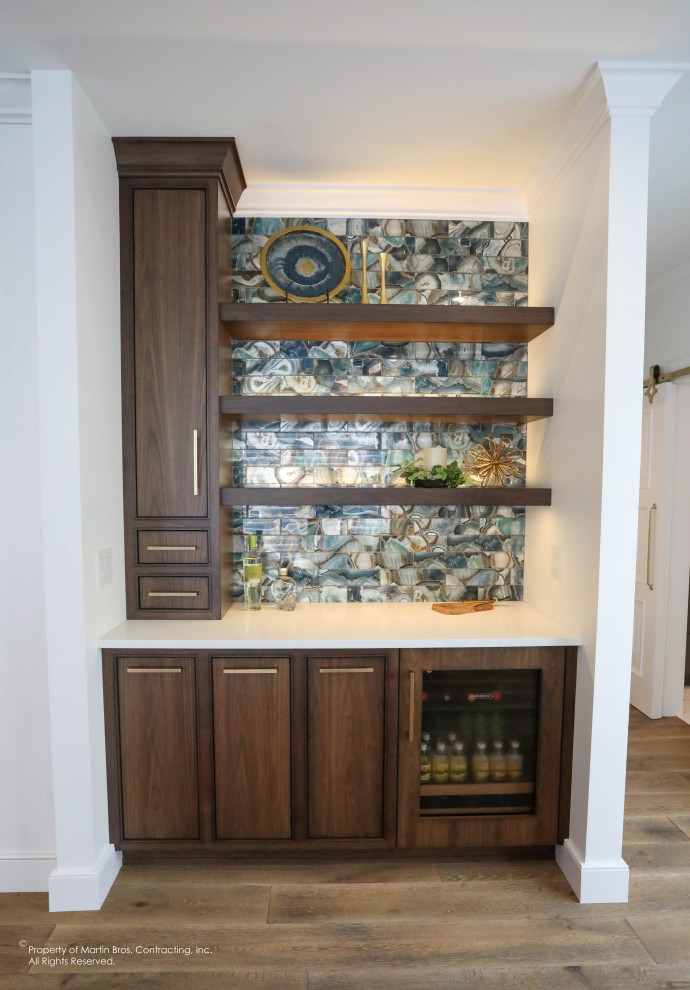 Photo of a small transitional single-wall home bar in Other with flat-panel cabinets, medium wood cabinets, quartzite benchtops, blue splashback, glass tile splashback, medium hardwood floors and white benchtop.