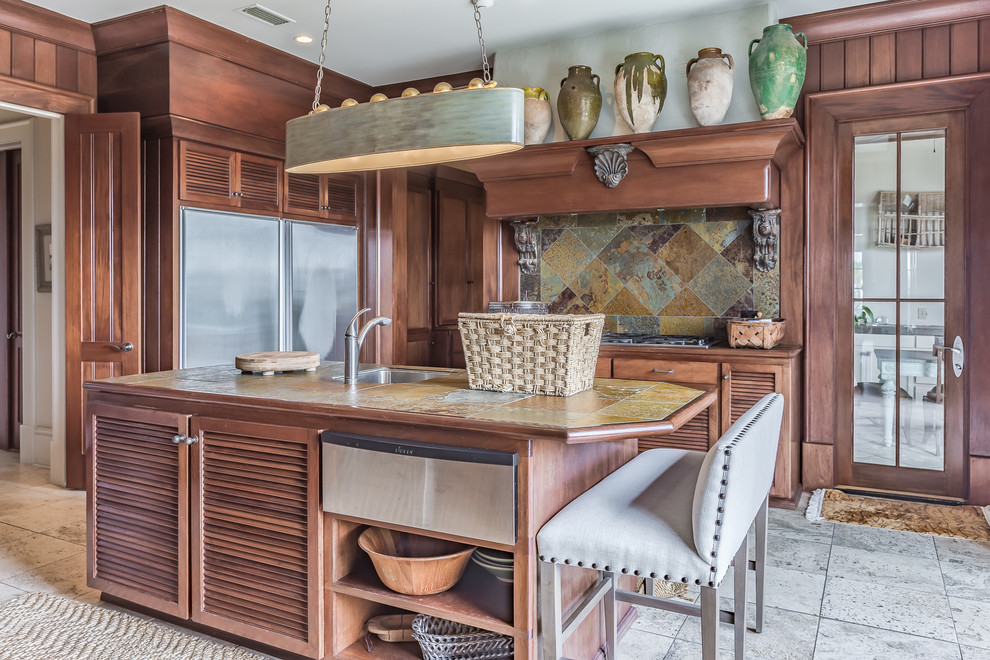 Photo of a large tropical kitchen in Miami with tile benchtops, stainless steel appliances, limestone floors, with island, a single-bowl sink, louvered cabinets, medium wood cabinets, multi-coloured splashback and slate splashback.
