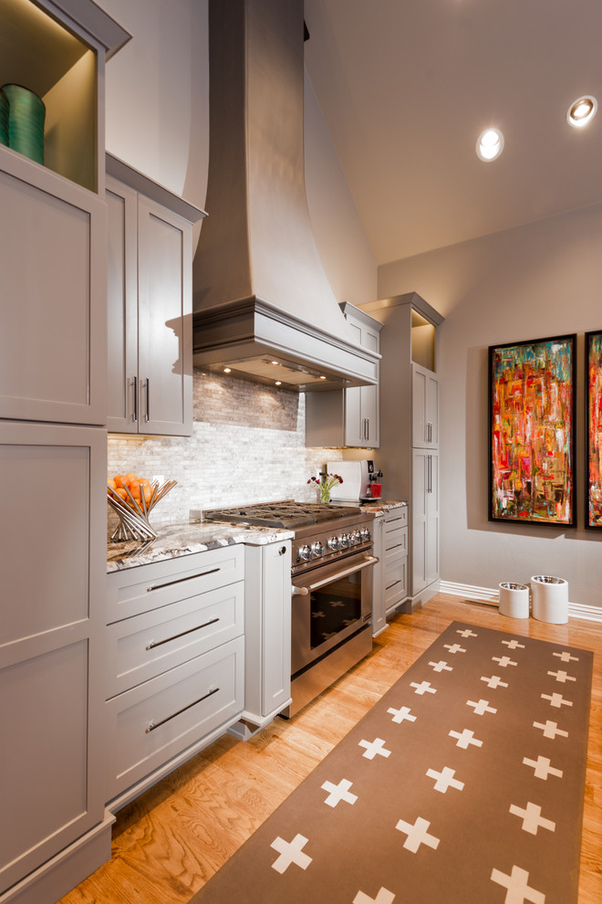 Example of a transitional kitchen design with shaker cabinets, gray cabinets, granite countertops, gray backsplash, stone tile backsplash and an island
