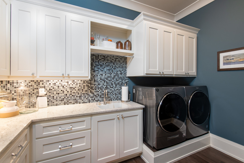 Idéer för mellanstora eklektiska l-formade vitt tvättstugor enbart för tvätt, med en undermonterad diskho, släta luckor, vita skåp, bänkskiva i kvarts, flerfärgad stänkskydd, stänkskydd i mosaik, blå väggar, laminatgolv, en tvättmaskin och torktumlare bredvid varandra och grått golv