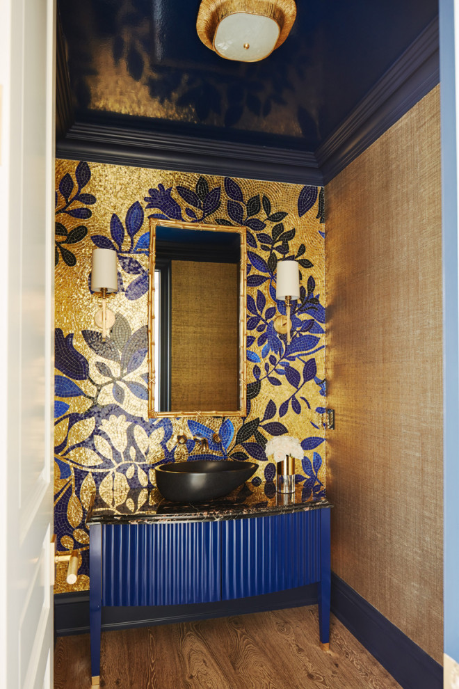 This is an example of an expansive traditional powder room in Toronto with a wall-mount toilet, a vessel sink, marble benchtops, multi-coloured benchtops, a built-in vanity, louvered cabinets, blue cabinets, multi-coloured tile, mosaic tile, multi-coloured walls, medium hardwood floors, brown floor and wallpaper.