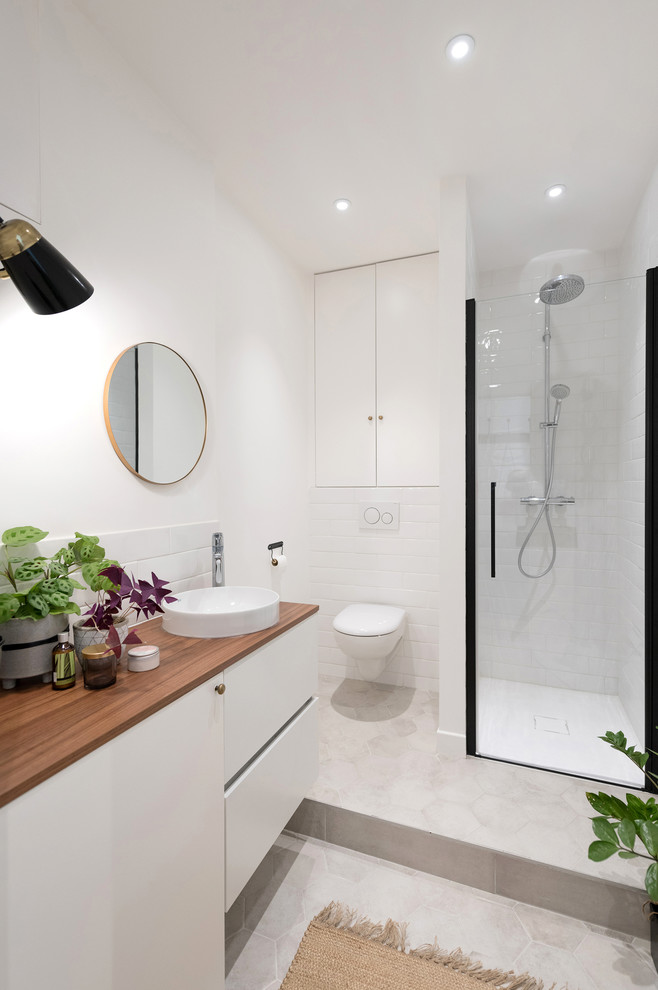 Inspiration for a scandinavian master bathroom in Lyon with flat-panel cabinets, white cabinets, a corner shower, a wall-mount toilet, white tile, white walls, a vessel sink, wood benchtops, beige floor, a hinged shower door and brown benchtops.