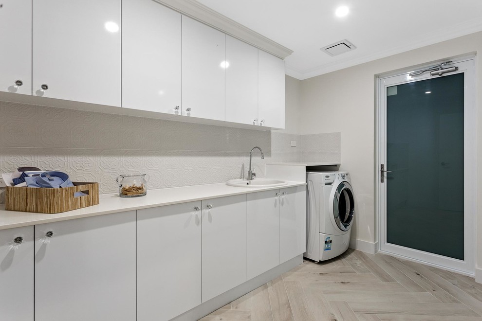 Inspiration for a beach style single-wall dedicated laundry room in Perth with a drop-in sink, white cabinets, solid surface benchtops, beige walls, light hardwood floors and beige benchtop.
