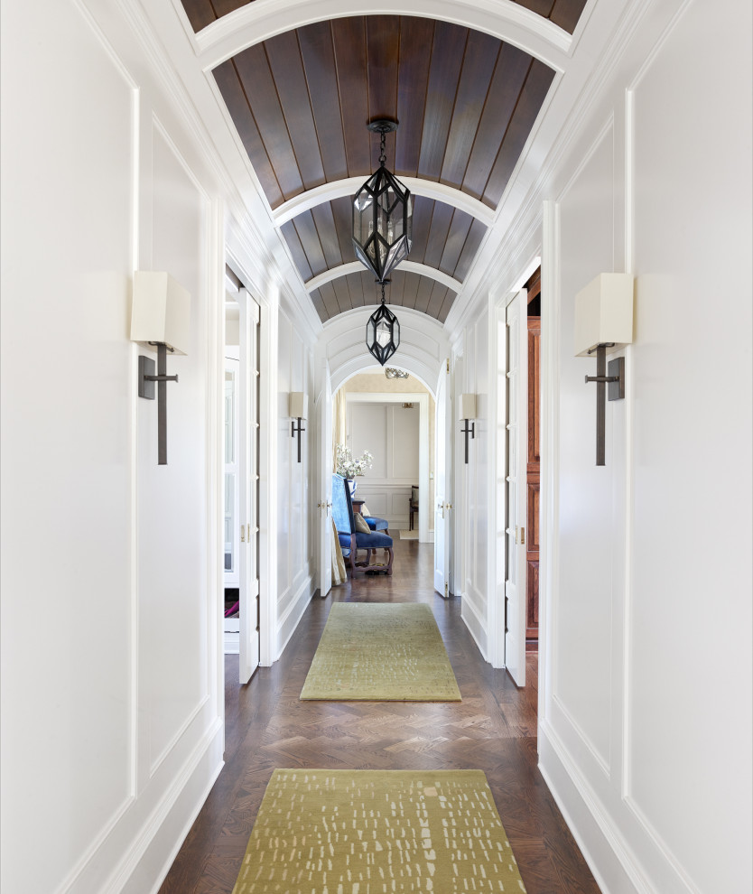 Cette photo montre un grand couloir chic avec un mur blanc, un sol en bois brun, un sol marron, un plafond voûté et du lambris.