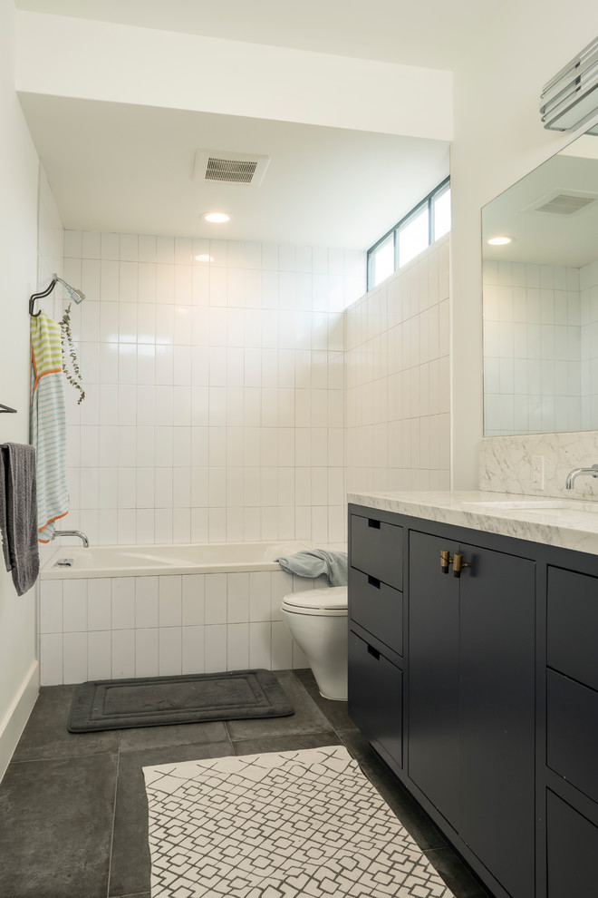 Design ideas for a mid-sized contemporary 3/4 bathroom in Houston with flat-panel cabinets, grey cabinets, a drop-in tub, a shower/bathtub combo, a one-piece toilet, white tile, porcelain tile, white walls, concrete floors, an undermount sink, marble benchtops, grey floor and a shower curtain.