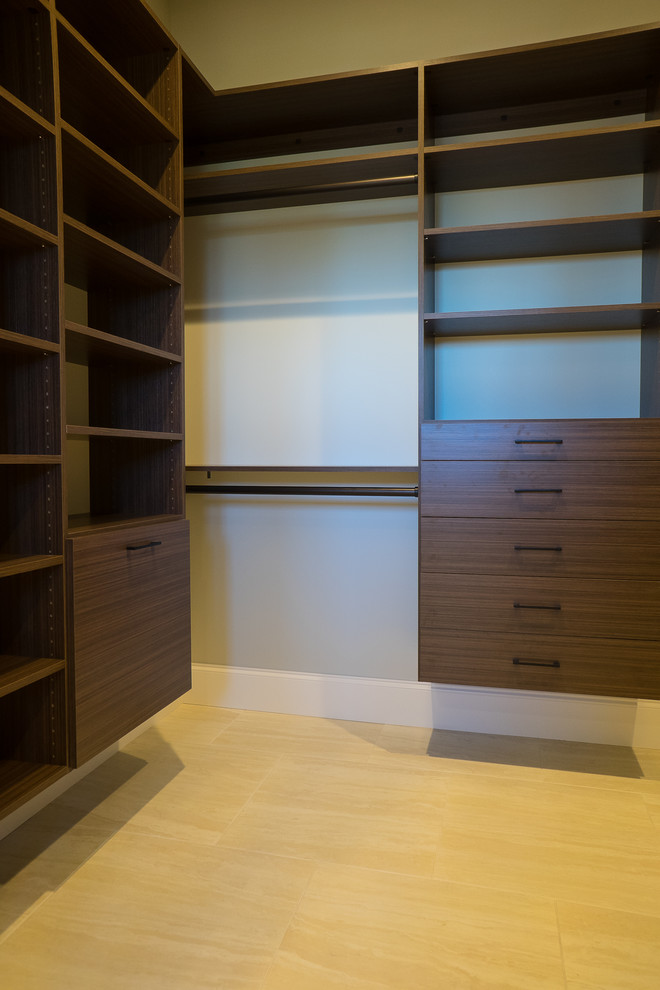 This is an example of a large mediterranean gender-neutral built-in wardrobe in Miami with flat-panel cabinets, dark wood cabinets, limestone floors and beige floor.