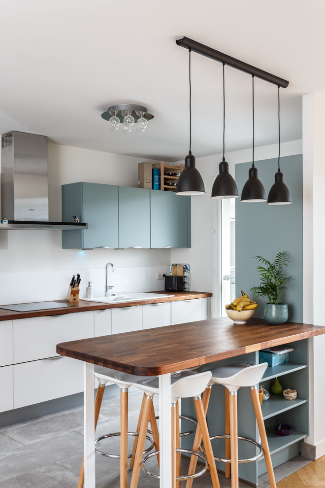 Photo of a scandinavian kitchen in Paris with a drop-in sink, flat-panel cabinets, blue cabinets, wood benchtops, white splashback, a peninsula and grey floor.