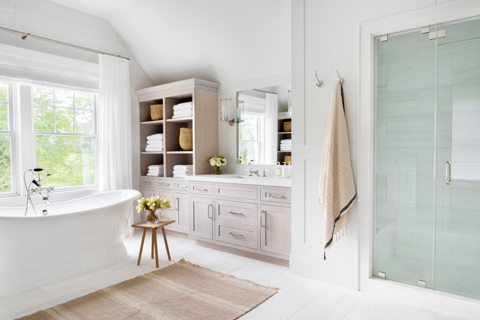 Inspiration for an expansive traditional master bathroom in New York with recessed-panel cabinets, light wood cabinets, a claw-foot tub, an alcove shower, a one-piece toilet, white tile, white walls, an integrated sink, marble benchtops, white floor, a hinged shower door and white benchtops.