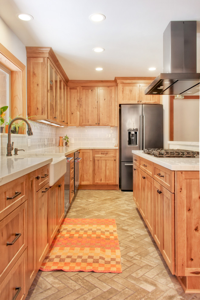 Inspiration for a mid-sized rustic l-shaped brick floor and brown floor open concept kitchen remodel with a farmhouse sink, shaker cabinets, medium tone wood cabinets, quartz countertops, blue backsplash, ceramic backsplash, stainless steel appliances, an island and white countertops