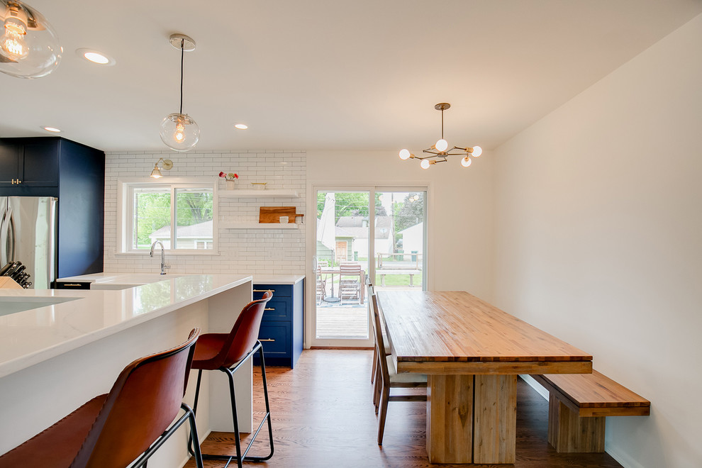Design ideas for a mid-sized contemporary galley eat-in kitchen in Minneapolis with a farmhouse sink, shaker cabinets, blue cabinets, quartz benchtops, white splashback, subway tile splashback, stainless steel appliances, medium hardwood floors, no island and brown floor.