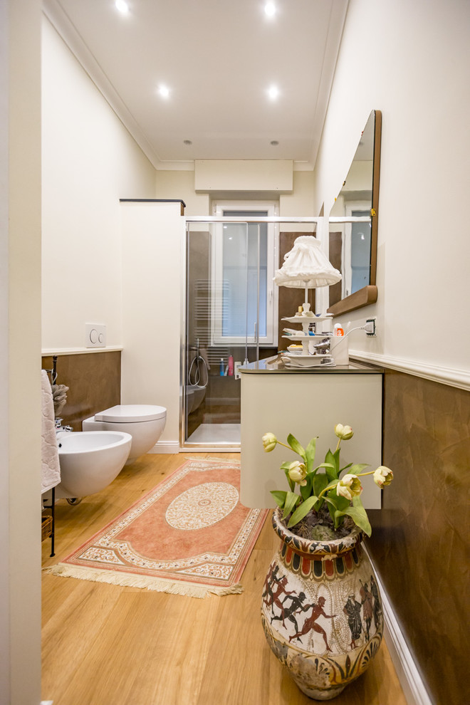 Mid-sized traditional master bathroom in Other with a double shower, a two-piece toilet, brown tile, brown walls, light hardwood floors, an integrated sink, glass benchtops, brown floor and a sliding shower screen.