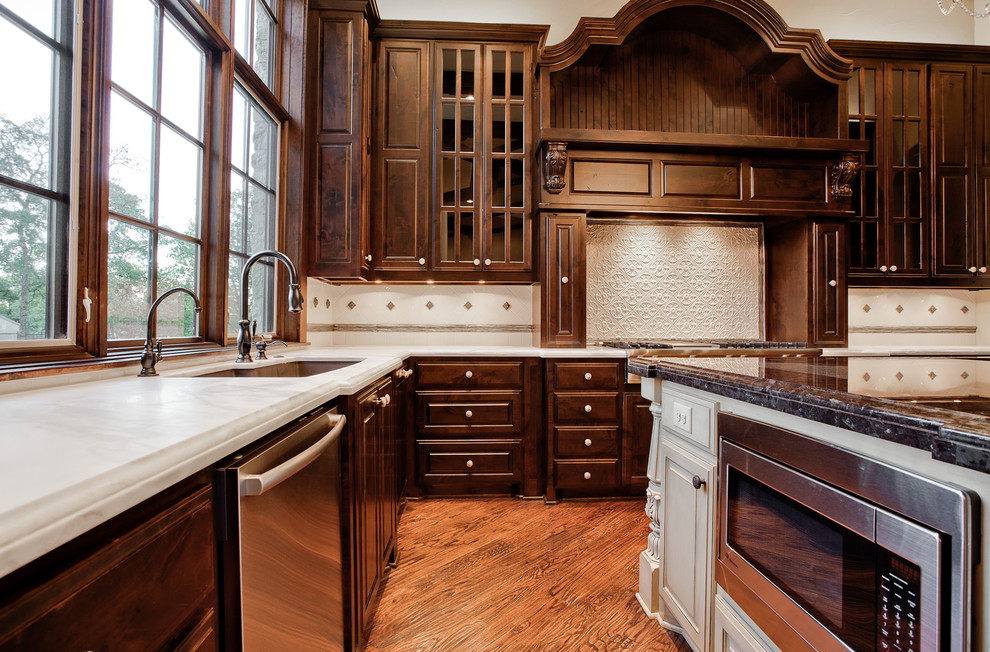Inspiration for a large traditional u-shaped separate kitchen in Dallas with an undermount sink, raised-panel cabinets, dark wood cabinets, marble benchtops, beige splashback, ceramic splashback, stainless steel appliances, medium hardwood floors, with island and brown floor.