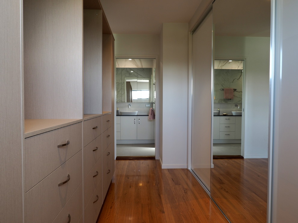 Mid-sized contemporary gender-neutral walk-in wardrobe in Brisbane with flat-panel cabinets, light wood cabinets, medium hardwood floors and beige floor.