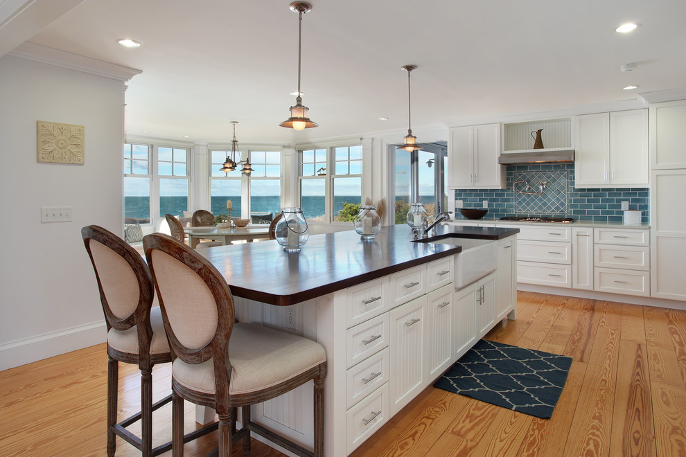 Photo of a beach style eat-in kitchen in Boston with a farmhouse sink, shaker cabinets, white cabinets, blue splashback, subway tile splashback, light hardwood floors, with island and grey benchtop.