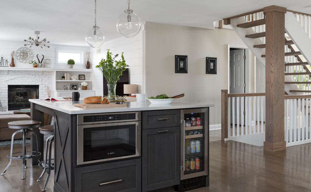 Mid-sized transitional u-shaped open plan kitchen in Chicago with a farmhouse sink, shaker cabinets, white cabinets, quartz benchtops, white splashback, marble splashback, stainless steel appliances, medium hardwood floors, with island, grey floor and grey benchtop.