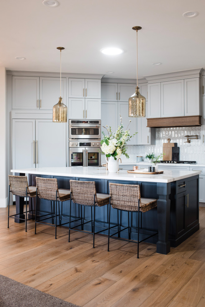 Inspiration for a mid-sized beach style eat-in kitchen in Phoenix with a farmhouse sink, recessed-panel cabinets, blue cabinets, marble benchtops, white splashback, stone tile splashback, panelled appliances, medium hardwood floors, with island, brown floor and white benchtop.