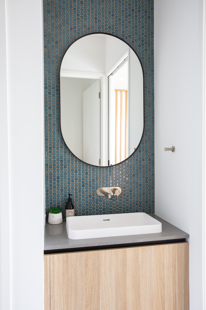 Réalisation d'un WC et toilettes design en bois clair avec un placard à porte plane, un carrelage bleu, mosaïque, un mur blanc, un lavabo posé et un plan de toilette gris.