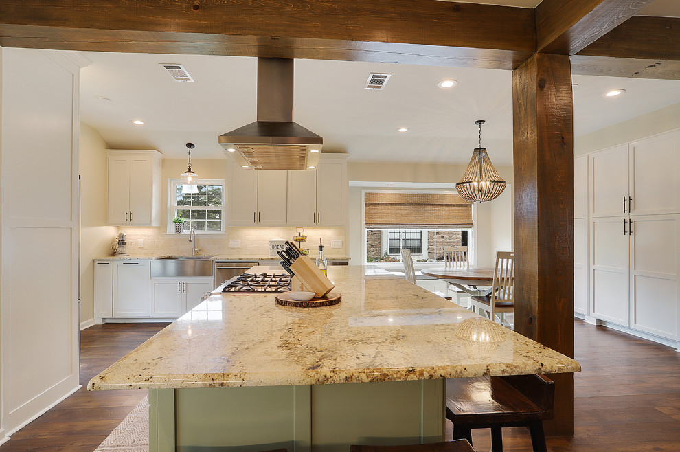 Photo of a mid-sized country single-wall open plan kitchen in New Orleans with a farmhouse sink, shaker cabinets, white cabinets, granite benchtops, white splashback, travertine splashback, stainless steel appliances, with island, brown floor, beige benchtop and dark hardwood floors.