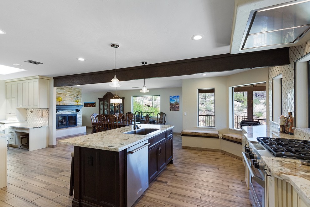 Example of a large transitional l-shaped porcelain tile and brown floor open concept kitchen design in Phoenix with an undermount sink, recessed-panel cabinets, dark wood cabinets, granite countertops, beige backsplash, ceramic backsplash, stainless steel appliances, an island and beige countertops