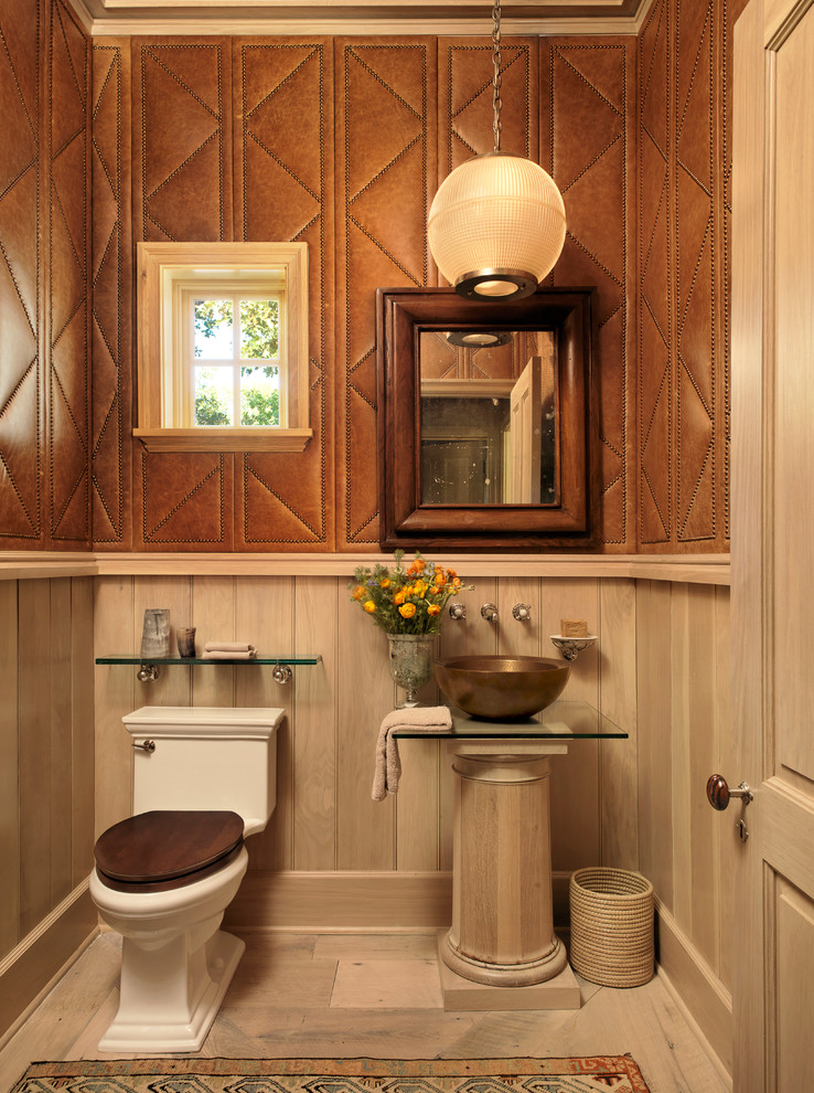 Photo of a country powder room in Austin with a vessel sink, glass benchtops, a two-piece toilet, brown walls and light hardwood floors.